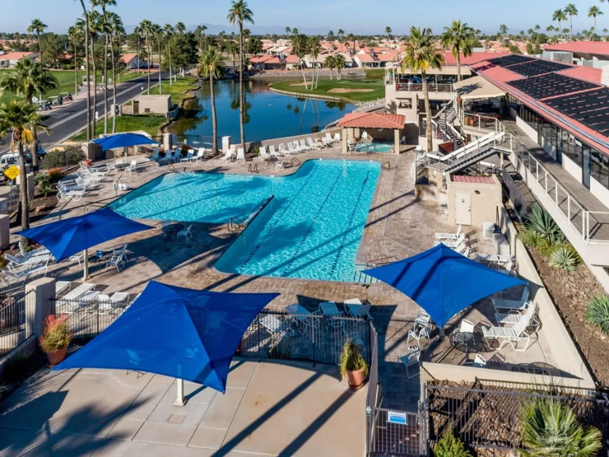 This image showcases a sparkling swimming pool beneath blue shade sails, surrounded by lush landscaping and palm trees. Lounge chairs and the inviting water set the scene for sunbathing, swimming, and socializing, exemplifying the resort's vibrant outdoor amenities.
