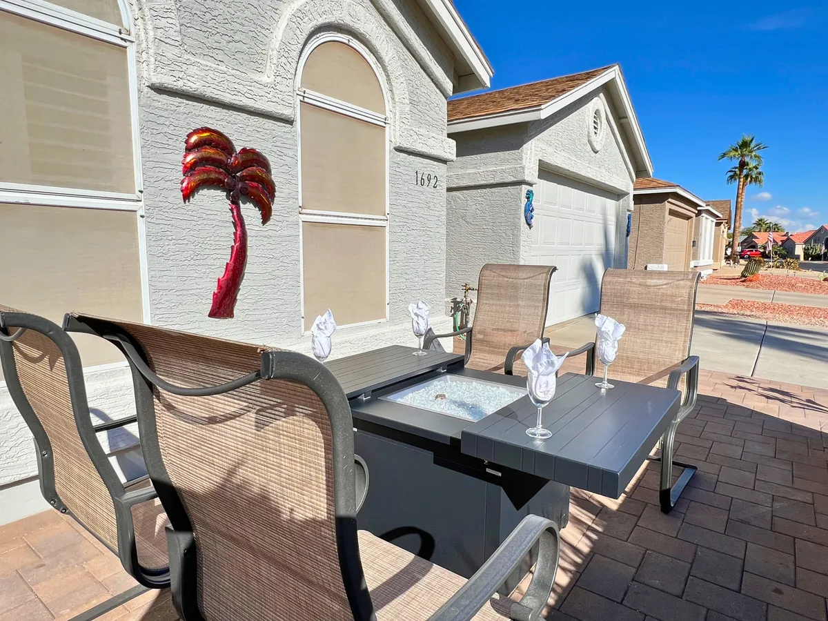 An outdoor dining area with a table set for gatherings, decorative palm tree art, and an inviting atmosphere ideal for socializing or relaxing. The setting suggests opportunities for enjoying meals outdoors and connecting with the community.
