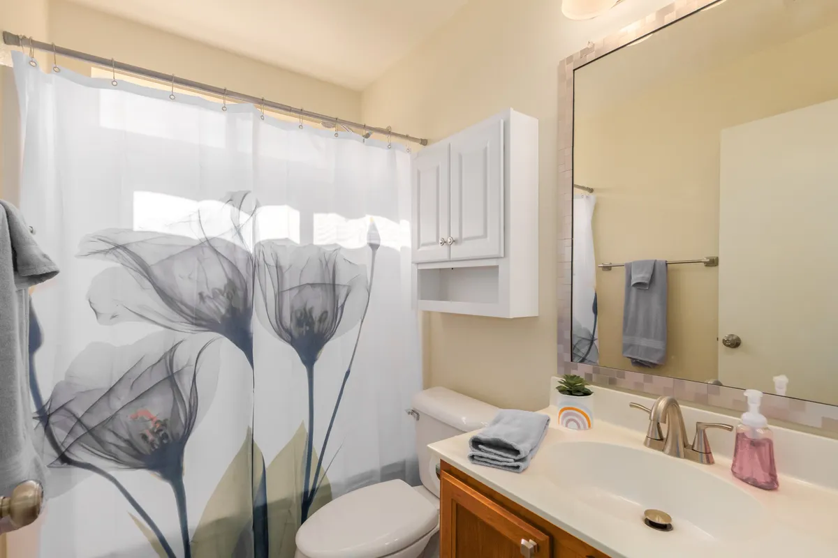 A bright and welcoming bathroom scene featuring a floral shower curtain, a well-lit vanity with a mirror, and a sink. The space is designed for comfort and relaxation, perfect for refreshing morning showers or winding down in the evening.