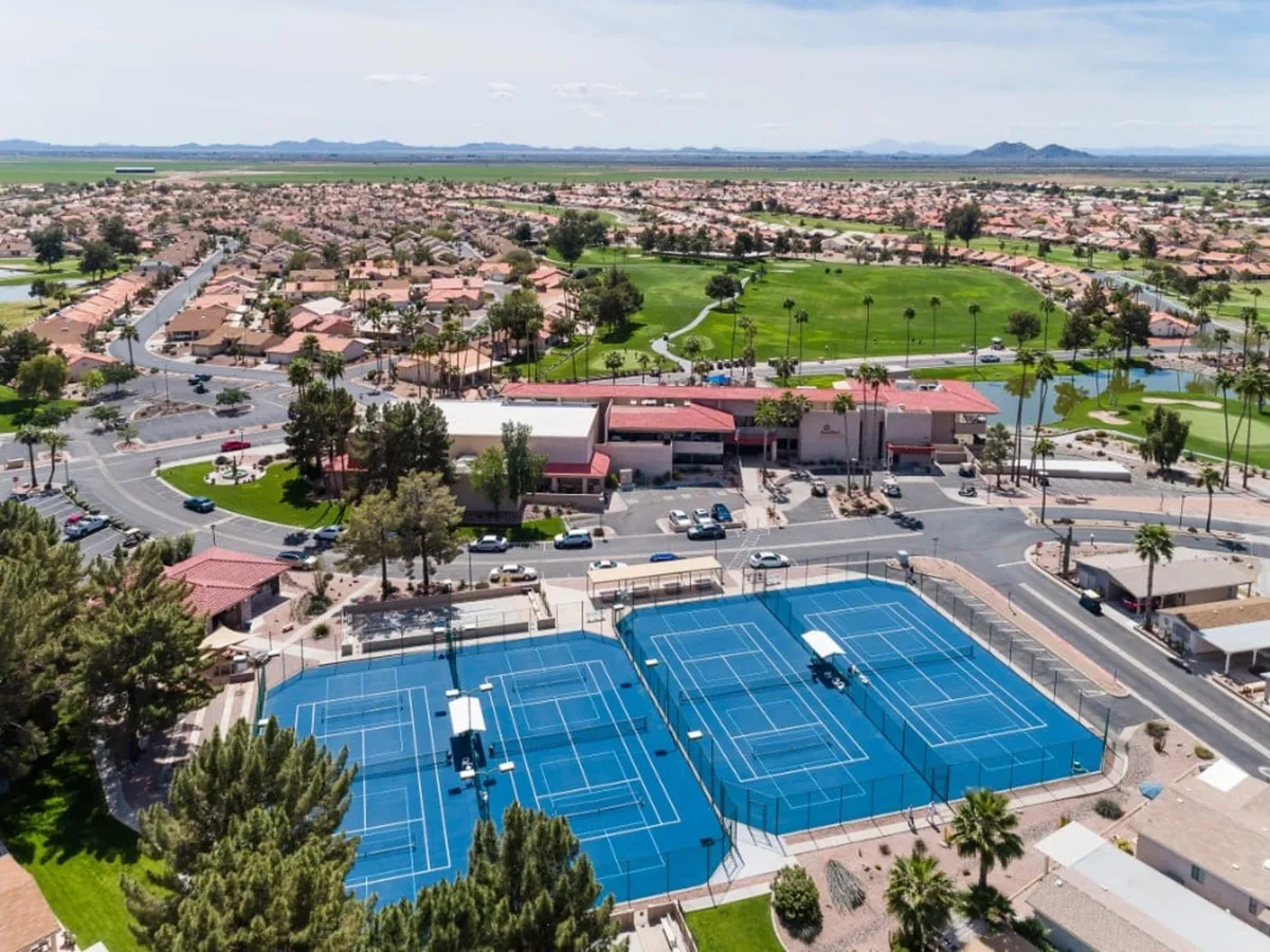 This exterior shot captures the tennis courts adjacent to the community center, with the surrounding residential area and golf course in view. The scene is bustling and energetic, emphasizing opportunities for sports, social gatherings, and the broader active lifestyle available to residents.