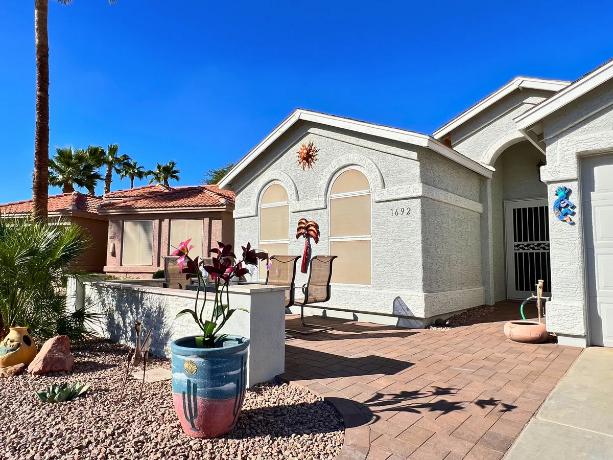This cheerful outdoor space features a decorative sun motif on the wall, colorful potted plants, and comfortable seating for relaxing or socializing. Bright sunlight fills the area, enhancing the vibrant, welcoming vibe.