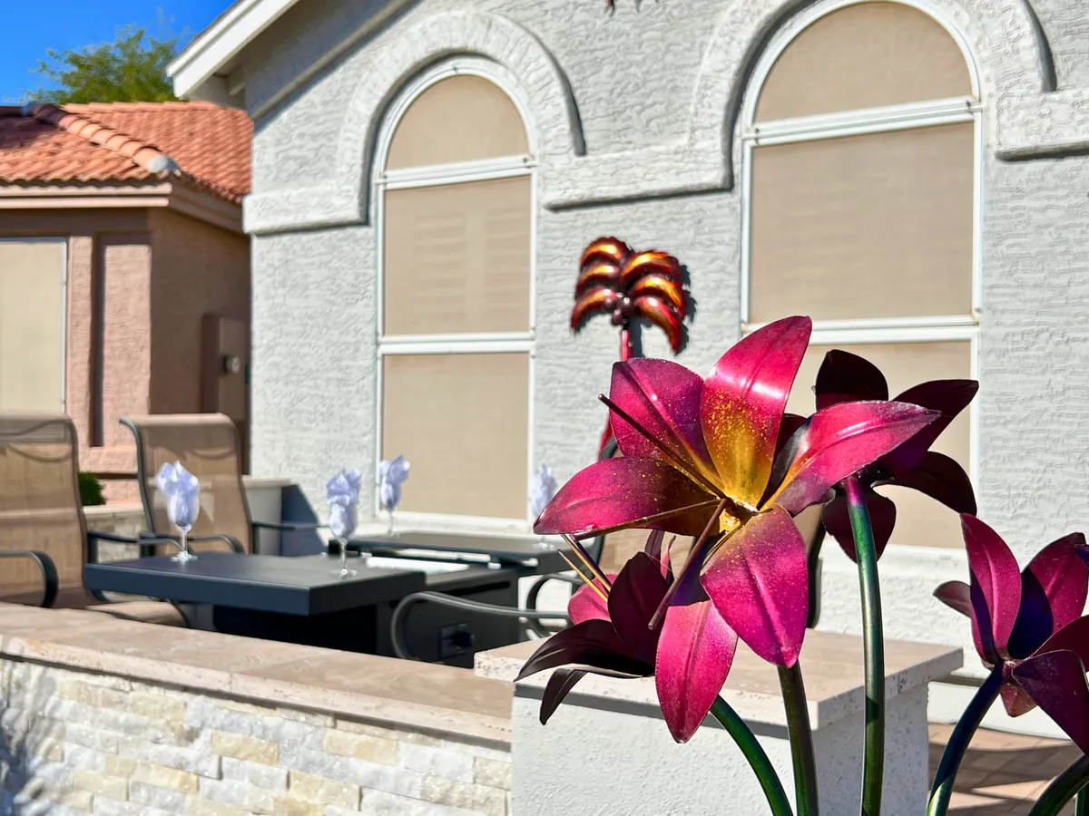A cheerful backyard scene features a dining table set amidst vibrant pink flowers and arched windows, evoking a sense of warmth and joy. The space is ideal for outdoor meals, with plenty of natural light and colorful garden accents enhancing the inviting ambiance.
