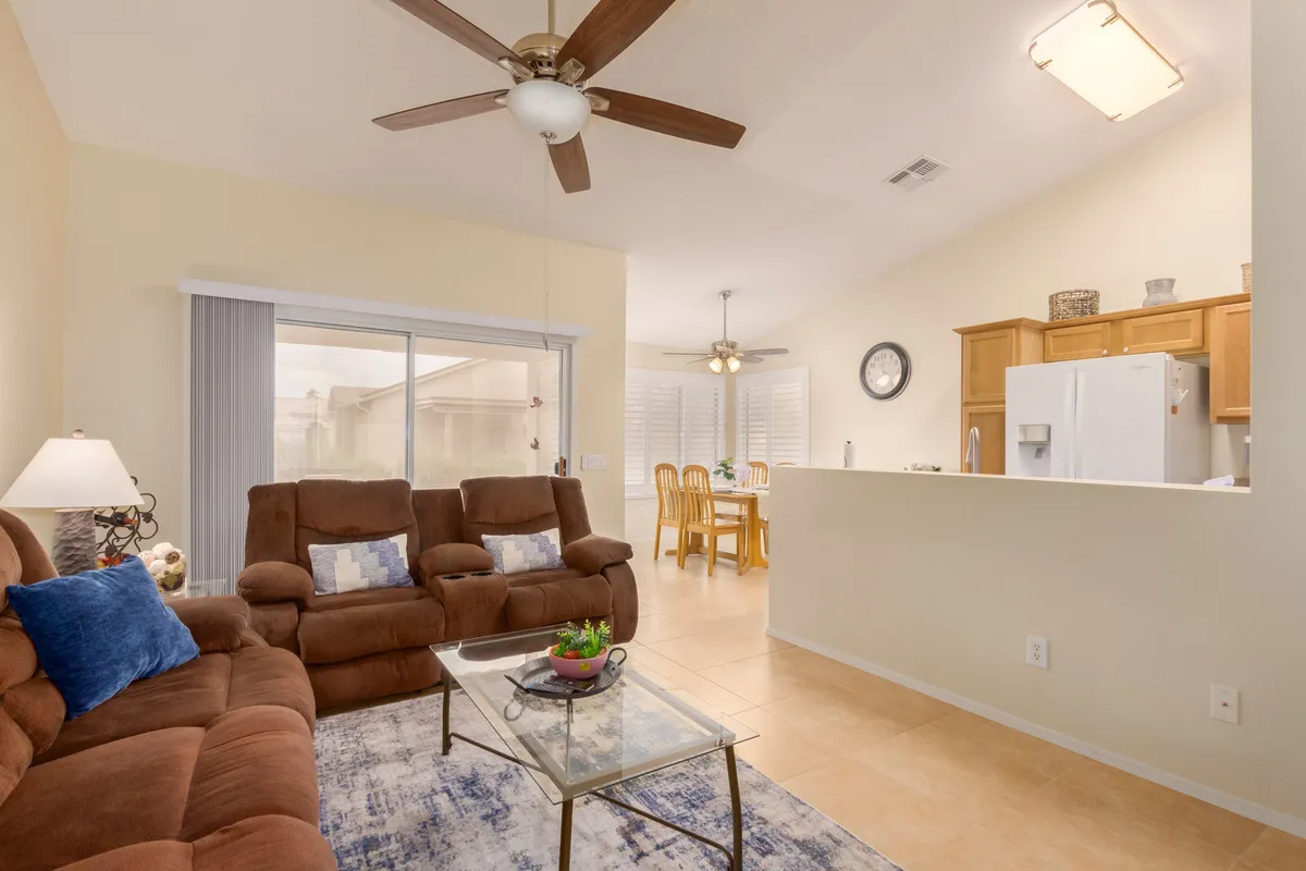 This image showcases a comfortable living room with plush brown sofas arranged around a glass coffee table, with a dining area visible in the background. The open layout and inviting furnishings are ideal for relaxation and group gatherings.