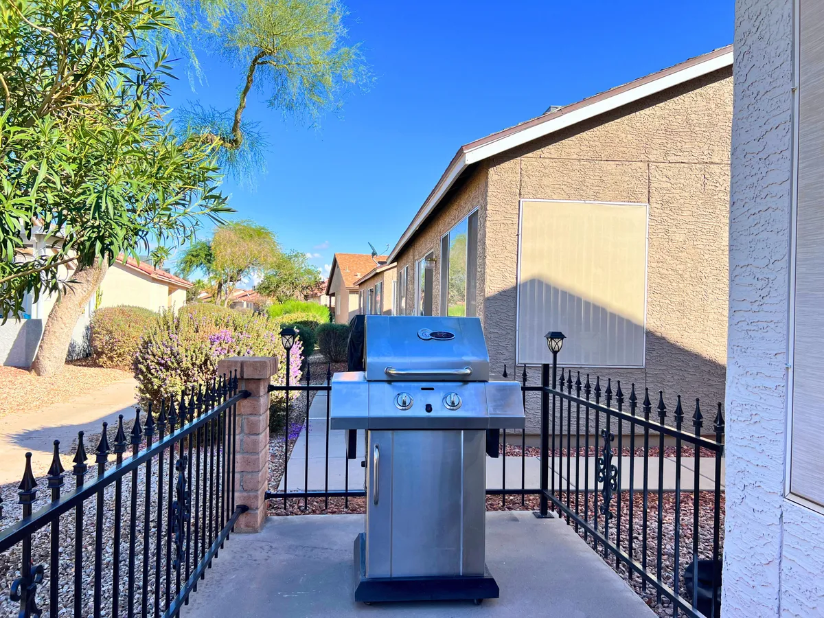 A grill is set against a backdrop of rich greenery and a decorative fence, signaling a space designed for barbecues and outdoor gatherings. The area is relaxed and private, encouraging memorable evenings spent enjoying good food and company.