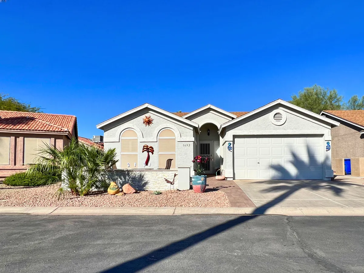 A cheerful and inviting entrance view featuring decorative elements, palm trees, and colorful potted plants. The front yard is arranged for social gatherings and morning relaxation, portraying the welcoming spirit and curb appeal of the Sunbird community.